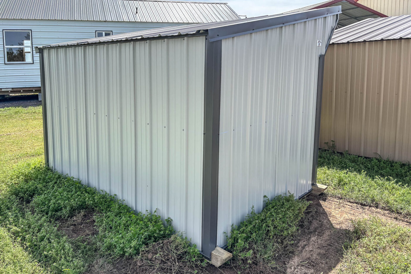 White and Gray metal loafing shed with fully enclosed back and sides, single-pitch roof, and standing on grassy terrain.