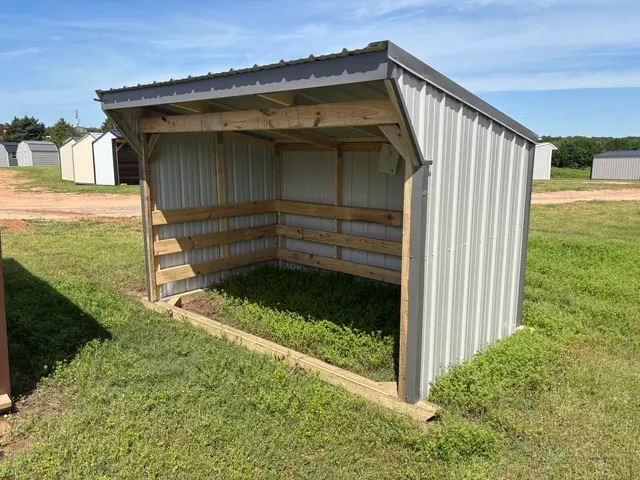 Gray metal loafing shed with wooden interior framing, three-sided coverage, and sloped roof over green grass.