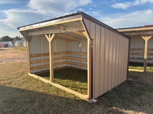 Tan loafing shed with a slanted roof, open front, and partial back and side coverage, resting on green grass.