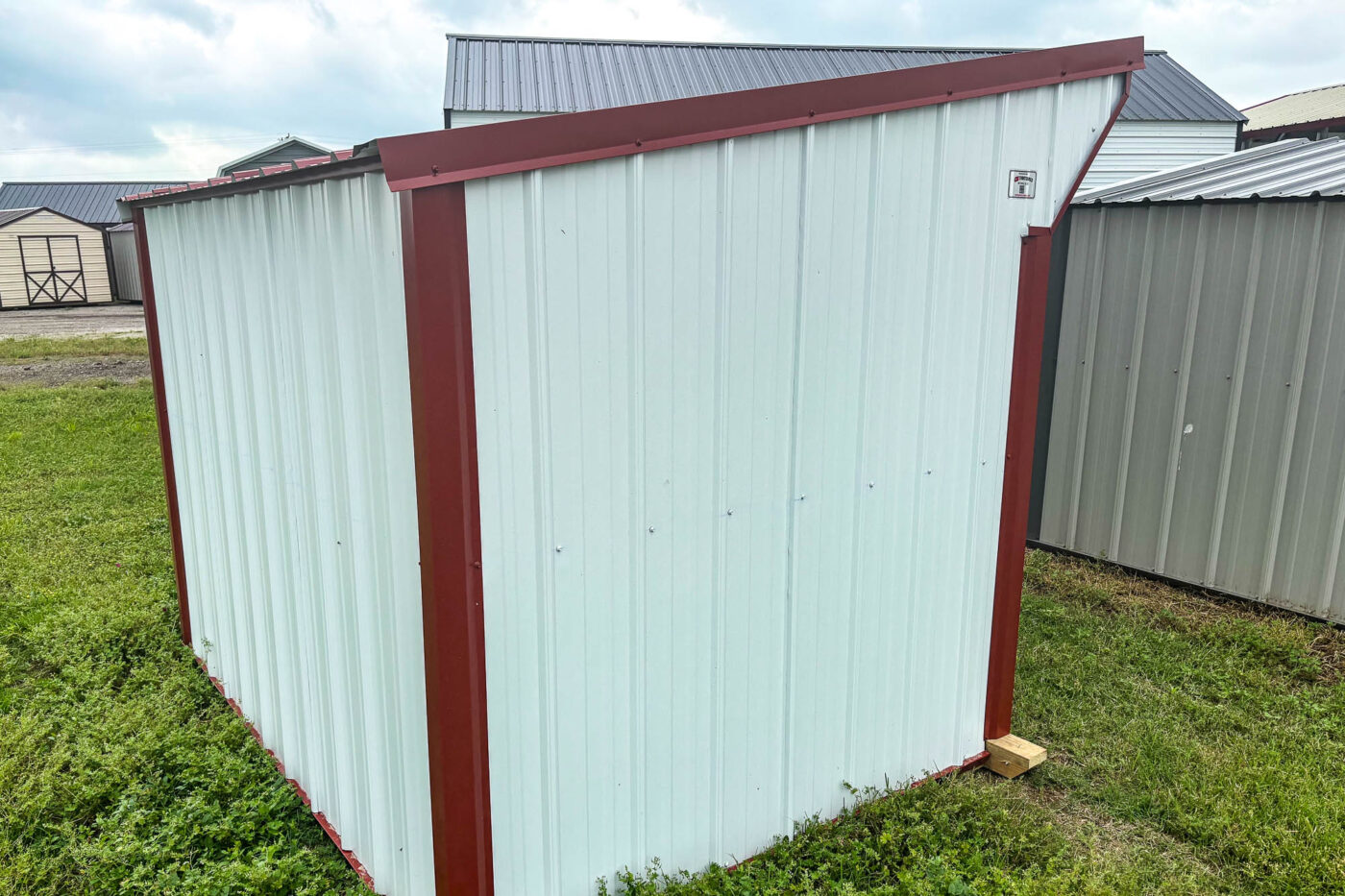 White loafing shed with red trim and sloped roof, metal siding, and enclosed back and sides on grassy ground.